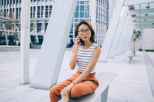Portrait of attractive female student with takeaway cup sitting outdoors and calling to customer service for checking account bank balance, beautiful Japanese woman making international conversation - Foto, Imagem