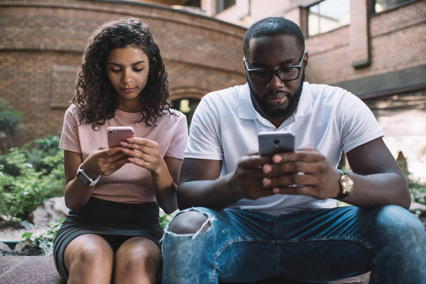 African American couple in love chatting with followers from web blog ignoring live communication with each other for using smartphone devices, concept of technology addiction and antisocial people - Photo, image