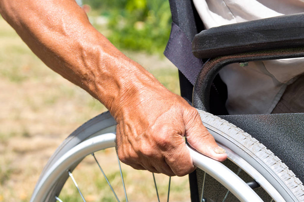 Vammainen mies istuu pyörätuolissa, pitää käsiään...
 - Valokuva, kuva
