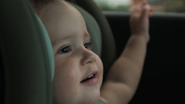 νήπιο κάθεται στο παιδικό κάθισμα ασφαλείας του αυτοκινήτου και κοιτάζει έξω από το παράθυρο - Φωτογραφία, εικόνα