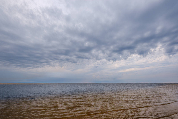 dramatyczne kolorowe chmury nad piaszczystą plażą nad morzem z niebieskimi s - Zdjęcie, obraz
