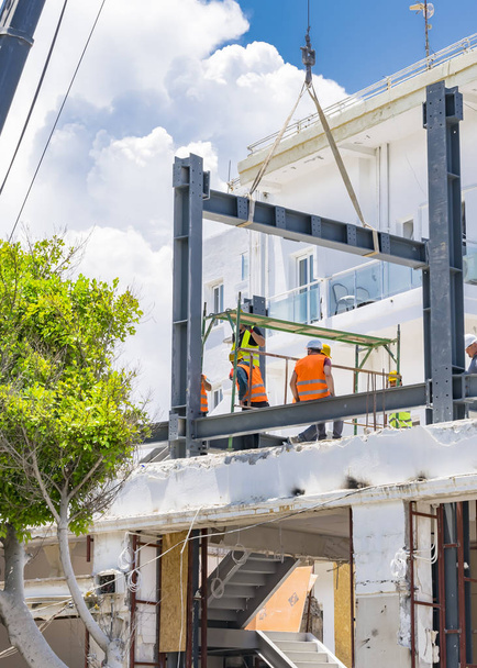 CHIPRE, Kyrenia - 10 de junio de 2019: Los constructores están construyendo un nuevo edificio en la azotea. Trabajadores vestidos con chalecos naranjas y cascos amarillos que trabajan en una obra de construcción
 - Foto, Imagen