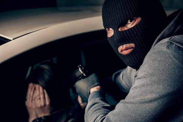 銃を持った仮面強盗が車の中で女性を脅す。強盗 - 写真・画像