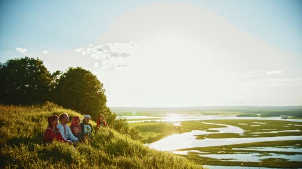 Lidé v tradičních ruských šatech sedícího na hřišti a mluvící-nádherná krajina při západu slunce - Záběry, video