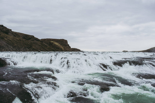 Cascada en Islandia. Salpicaduras blancas, agua turquesa y roca negra bajo el cielo gris. Primavera
 - Foto, imagen