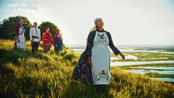 Mladí lidé v tradičních šatech, kteří stojí na hřišti a užívají si výhled na západ slunce - Záběry, video