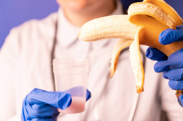 Naislääkärit kädet lääketieteellisissä sinisissä käsineissä, joissa on muovisäiliö, jossa on sperma ja banaani
. - Valokuva, kuva
