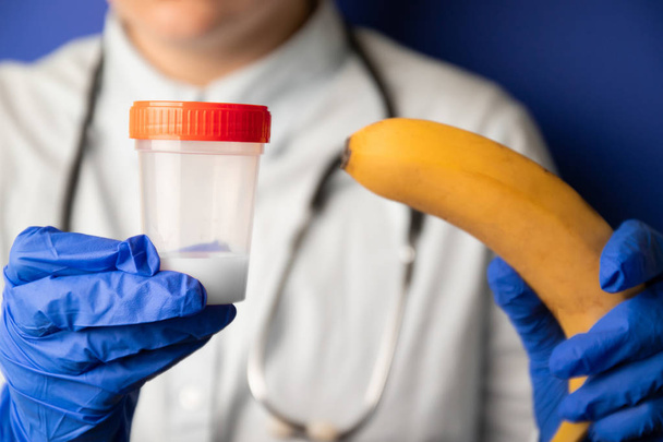 Naislääkärit kädet lääketieteellisissä sinisissä käsineissä, joissa on muovisäiliö, jossa on sperma ja banaani
 - Valokuva, kuva