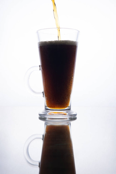 Dark beer is poured into a mug on a white background.   - 写真・画像