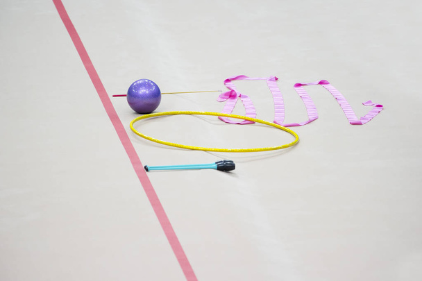 Спортивне обладнання для художньої гімнастики лежить на краю килима в тренажерному залі. Клуби художньої гімнастики, м'яч, обруч
. - Фото, зображення
