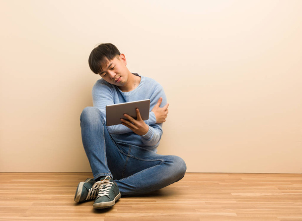 junger Chinese sitzt mit seinem Tablet und umarmt sich - Foto, Bild