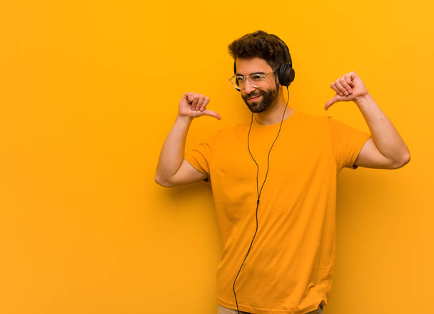 Young man listening to music pointing fingers, example to follow - Фото, изображение