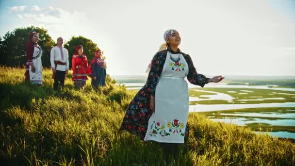 Mladí lidé v ruském tradičním oblečení stojící na hřišti a žena zpívající písničku, která se těší pohledu na západ slunce - Záběry, video