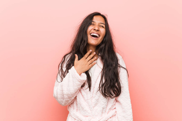 Młoda indyjska kobieta ubrana w piżamę śmieje się głośno trzymając rękę na klatce piersiowej. - Zdjęcie, obraz
