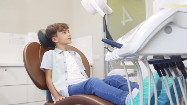 Mooie jonge jongen zittend in tandheelkundige stoel wachten op tanden onderzoek - Video