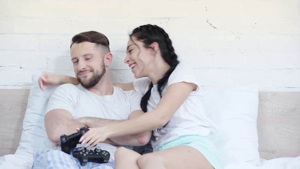 KYIV, UKRAINE - MARCH 21, 2019: happy woman gesturing while playing video game and winning near man with crossed arms, then kissing in bedroom  - Video
