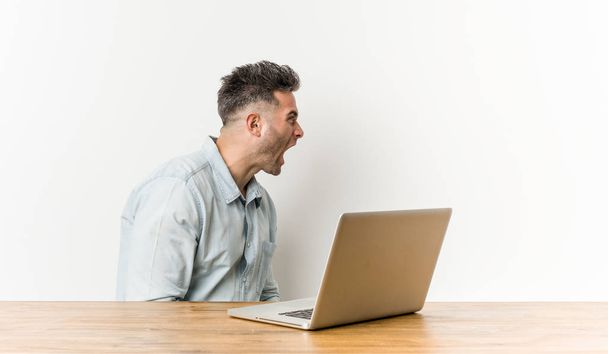 Młody przystojny człowiek pracujący z jego laptop krzycząc w kierunku przestrzeni kopiowania - Zdjęcie, obraz