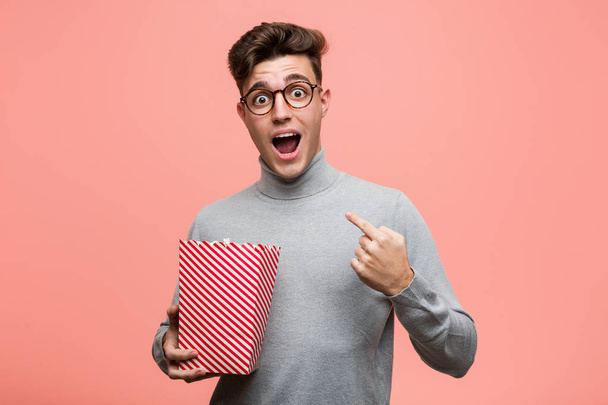Young intellectual man holding a popcorn bucket showing fist to camera, aggressive facial expression. - 写真・画像