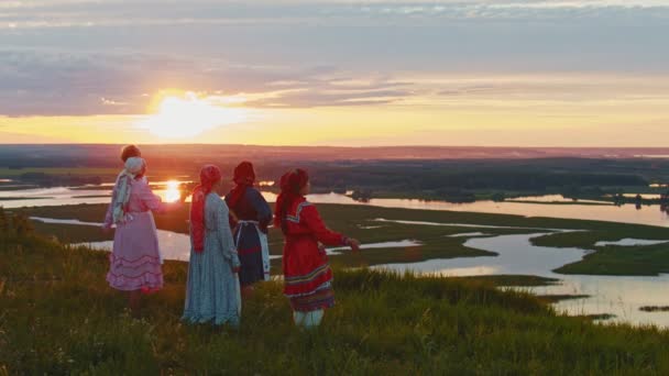 Mladí lidé na ruském tradičním oblečení stojící na hřišti a vychutnávají si výhled na západ slunce a na malé ostrovy - Záběry, video