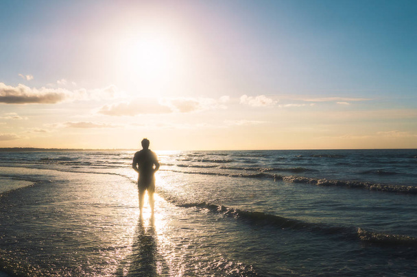 Silhouette of a young man standing on the seashore facing the sun. Outdoors, summer, freedom concept with copy space. - Foto, Imagen
