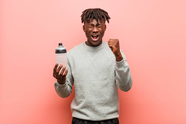 Fiatal fitness fekete férfi, aki egy vizes palackot ujjongott gondtalan és izgatott. Győzelmi koncepció. - Fotó, kép