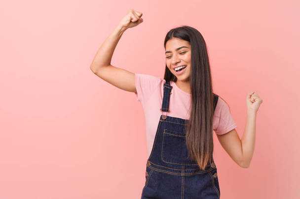 Young pretty arab woman wearing a jeans dungaree raising fist after a victory, winner concept. - Foto, imagen
