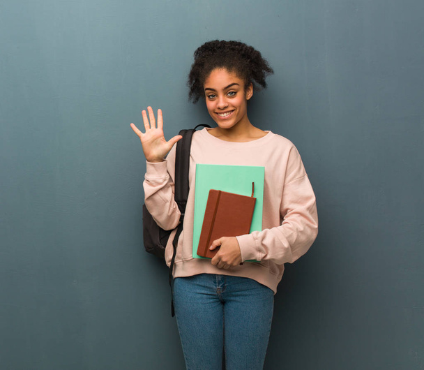 Nuori opiskelija musta nainen näyttää numero viisi. Hänellä on kirjoja.
. - Valokuva, kuva