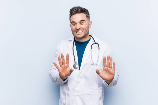 Young handsome doctor man rejecting someone showing a gesture of disgust. - Foto, Imagen