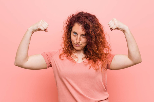 Nuori luonnollinen ja aito punapää nainen osoittaa voimaa ele aseita, symboli naisellinen voima
 - Valokuva, kuva