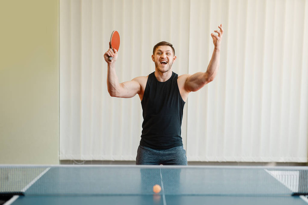 El hombre con raqueta en la mano gana el torneo de ping pong en interiores. Hombre en ropa deportiva, entrenamiento en club de tenis de mesa
 - Foto, Imagen