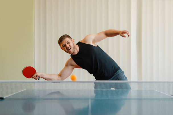 Homem com raquete de ping pong joga a bola fora, imagem em ação, treino dentro de casa. Masculino em sportswear, treinamento em clube de tênis de mesa
 - Foto, Imagem