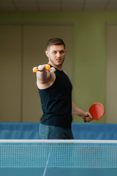 Człowiek z rakieta trzyma ping pong piłki między palcami, trening w pomieszczeniu. Męska osoba w odzieży sportowej, trening w klubie tenisa stołowego - Zdjęcie, obraz