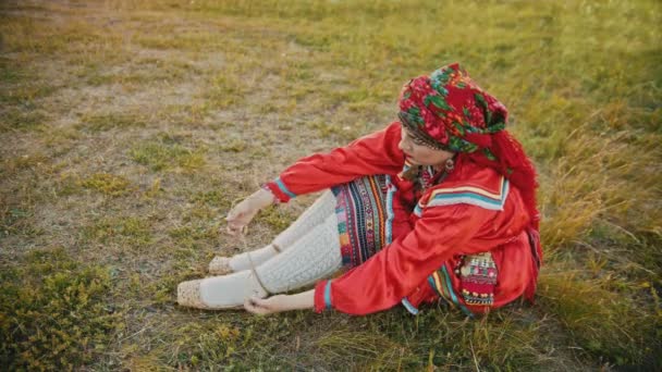 Μια γυναίκα σε Ρωσικά κόκκινα λαϊκά ρούχα που βάζουν στα παπούτσια-κάθονται στο γήπεδο - Πλάνα, βίντεο