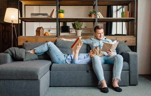 自宅で快適なソファで休んでいる若い愛のカップル。夫と妻はリビングルームでリラックス。一緒に幸せな家族、ソファで本を読む男女 - 写真・画像