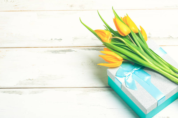greeting card yellow tulips on turquoise gift box on a white wooden background. Scandinavian style, place for text. - Photo, Image