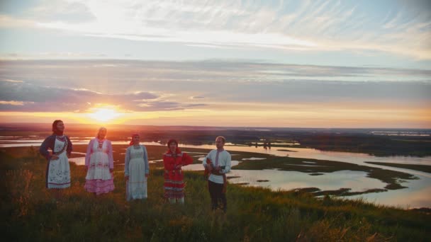 Mladí lidé v ruském tradičním oblečení stojící na poli na pozadí nádherného západu slunce a zpěvu - Záběry, video