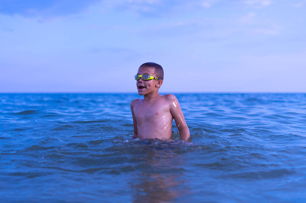 A 10-year-old boy swims in the sea at dawn with glasses for swim - Photo, Image