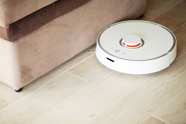 Casa Inteligente. Aspirador robot funciona en el suelo de madera en una sala de estar. - Foto, Imagen