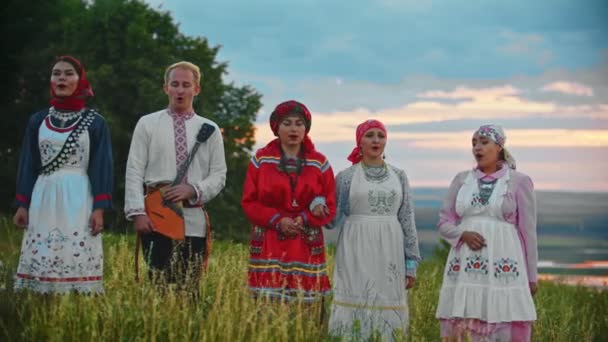 Lidé v tradičních lidových šatech, kteří chodí po hřišti a zpívají píseň k západu slunce - Záběry, video