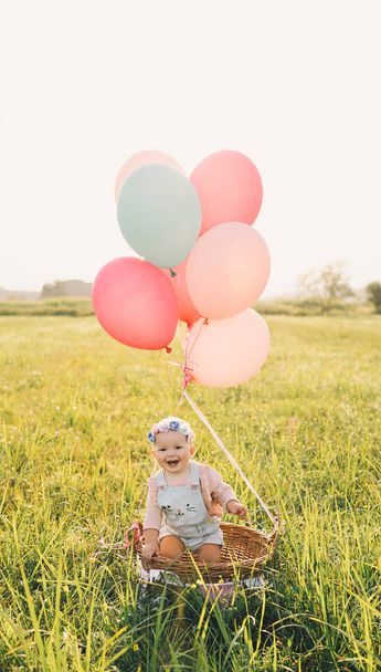 Baby girl in wicker basket with balloons on nature at summer - Photo, image