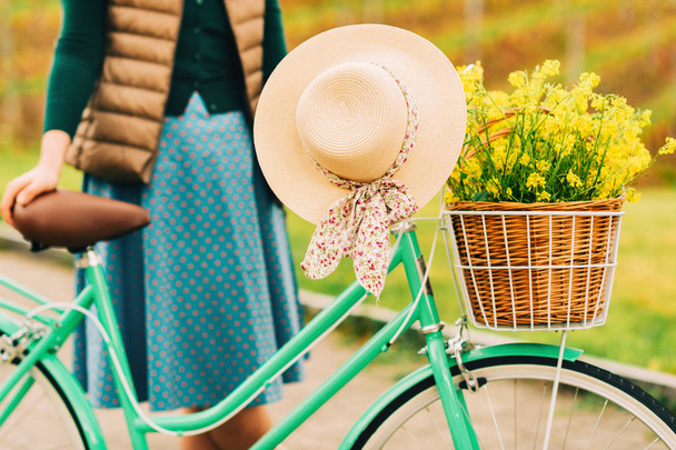 Woman holding vintage bicycle with hanging summer hat, yellow rapeseed flowers in wicker basket - Foto, Imagem