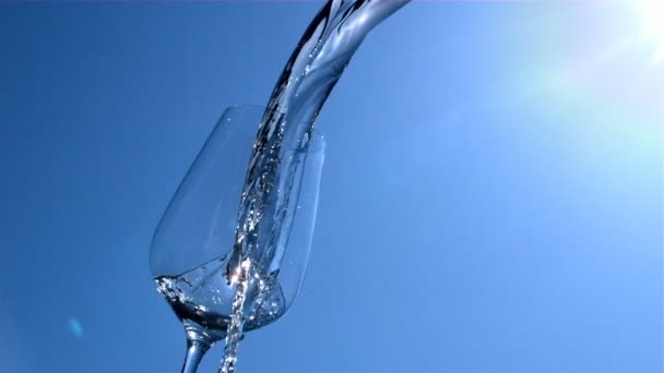 Vesi valuu lasiin, jossa on sininen taivas ja auringonpaiste taustalla hitaassa liikkeessä
 - Materiaali, video