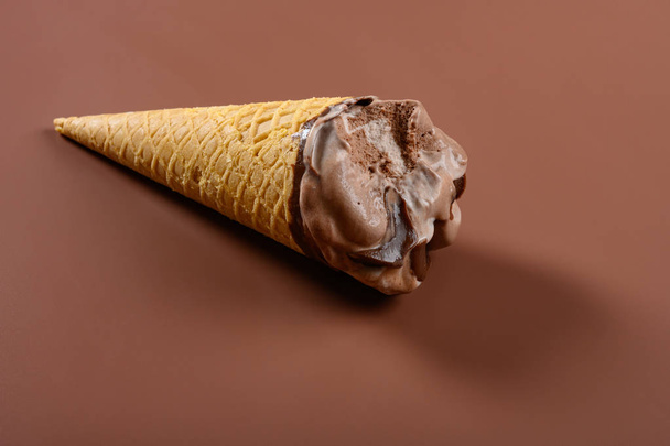 vista lateral de café y chocolate sabor cono de helado con un par de bocados sobre fondo marrón
 - Foto, imagen