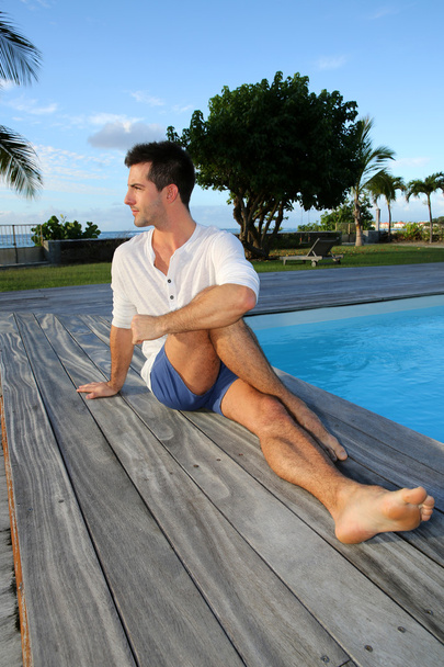 Young man doing stretching exercises on pool deck - Fotó, kép
