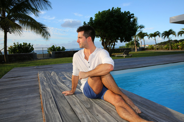 Young man doing stretching exercises on pool deck - Фото, изображение