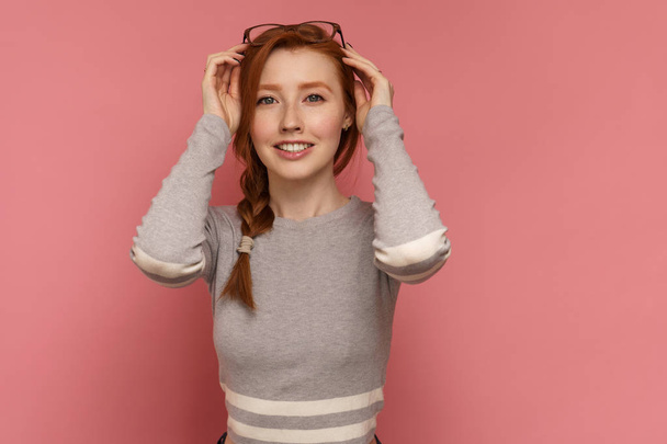Red-haired young woman smiles joyfully at the camera putting the glasses on her head - Фото, зображення