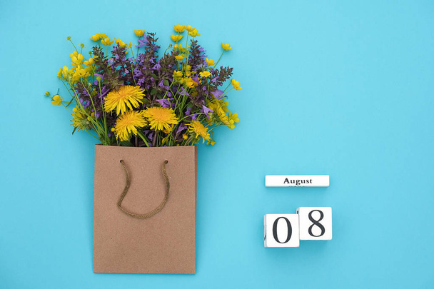 Wooden cubes calendar August 8 and field colorful rustic flowers in craft package on blue background. Greeting card Flat Lay Concept Hello August Template with copy space for text and design - Fotoğraf, Görsel