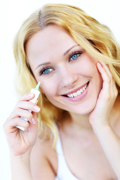 Smiling woman applying concealer in front of mirror - Photo, Image