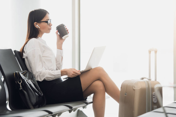 Young businesswoman in the airport, using laptop and drinking coffee, travel, business trip and active lifestyle concept - Foto, afbeelding
