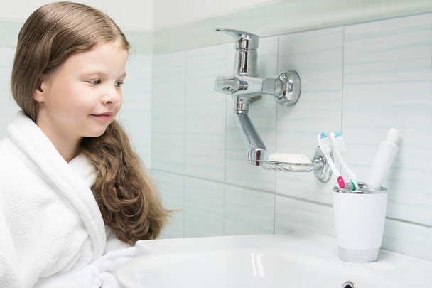 a girl in a bathrobe came to the bathroom to brush her teeth - Foto, immagini